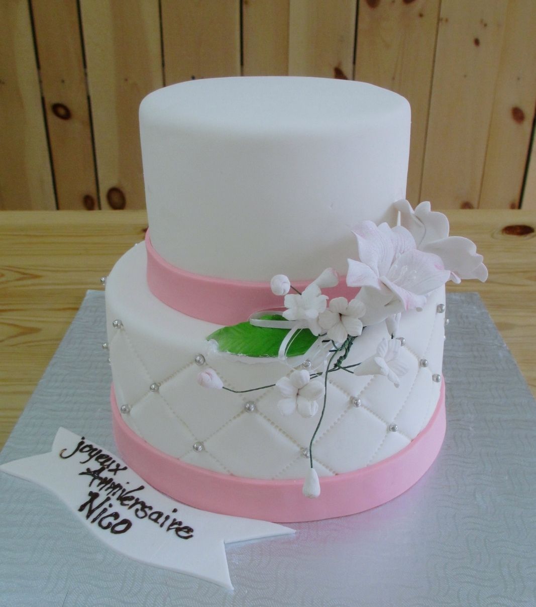 Gâteau d'anniversaire sur mesure de Nico: gâteau de 2 étages avec une couverture en fondant, une base à effet matelassé (quilting) ornementée de perles argentées et décoré d'un bouquet de fleurs en sucre sculptées.