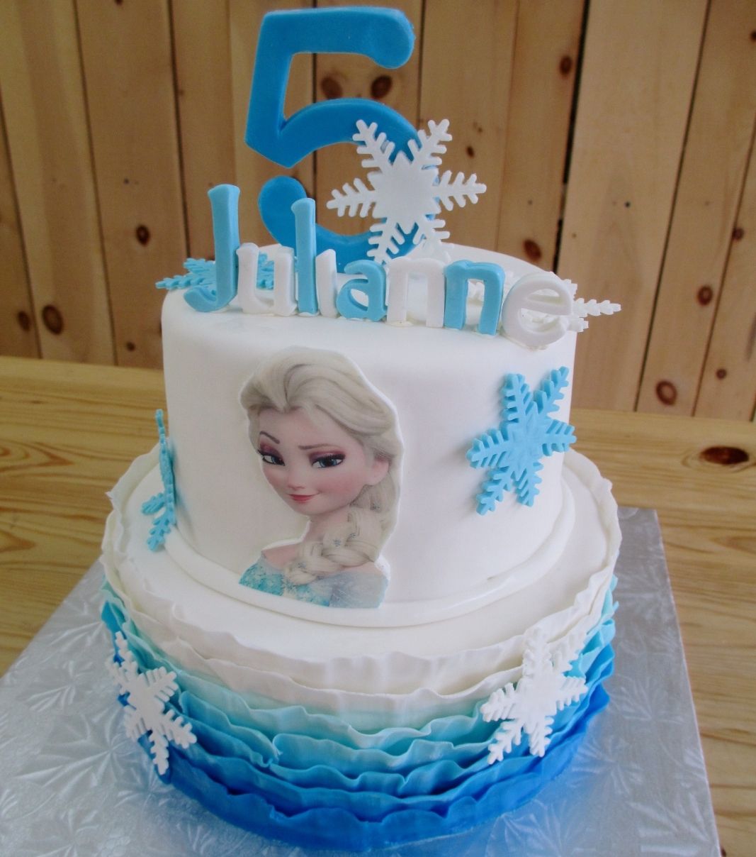Gâteau d'anniversaire sur mesure des 5 ans de Julianne: gâteau de 2 étages à thématique Reine des Neiges avec la base en texture plissée (ruffle) dégradée de bleu à blanc et décoré avec des flocons de neige en fondant et une impression comestible.