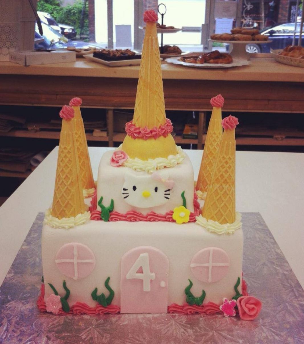 Gâteau d'anniversaire sur mesure des 4 ans de Rose: gâteau de 2 étages en forme de château à thématique de princesse Hello Kitty avec une couverture en fondant rose et décoré de cornets de crème glacée.