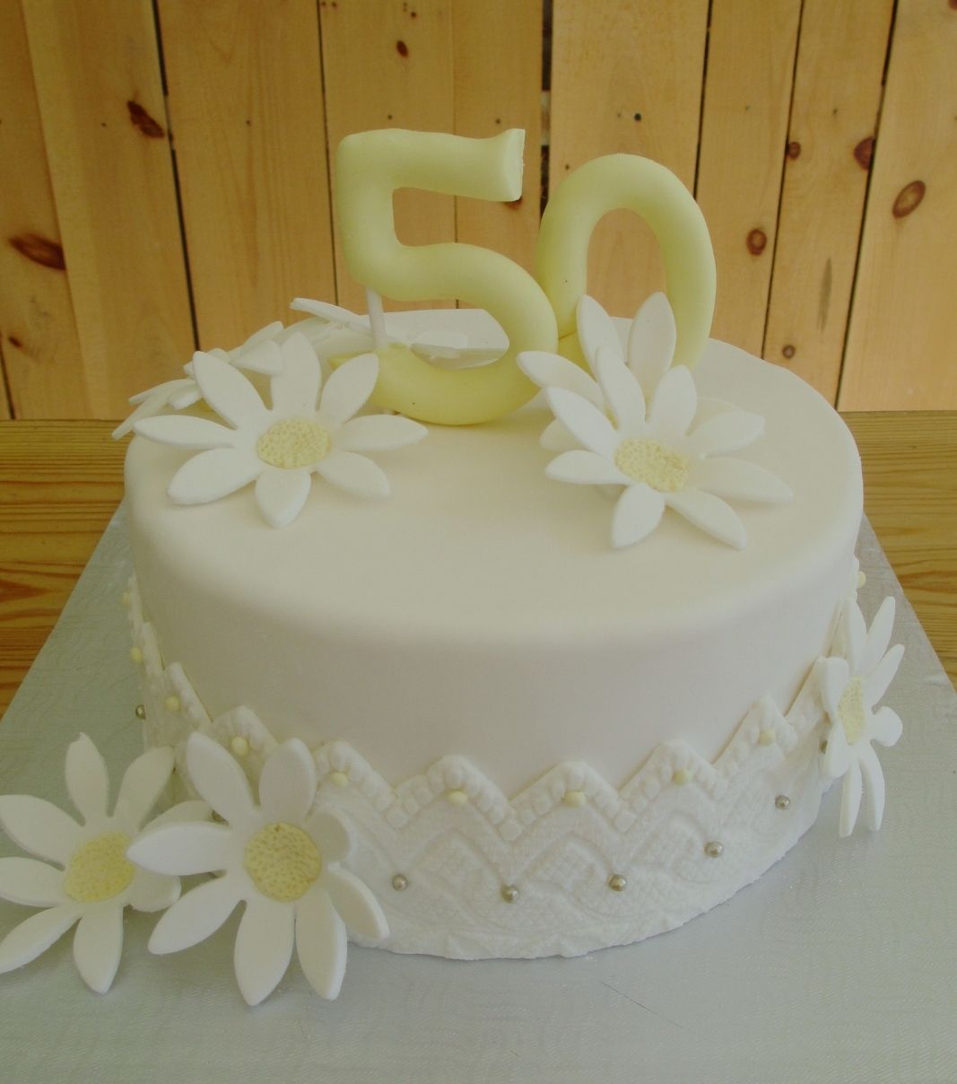 Gâteau d'anniversaire sur mesure de 50 ans: gâteau blanc sur blanc à thème fleur de marguerite avec une bordure en fondant à texture de dentelle.