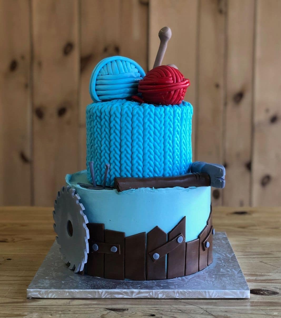 Gâteau d'anniversaire sur mesure de la même de Vincent: gâteau de 2 étages à thématique de tricot avec une couverture en fondant et décoré d'une scie ronde, d'une aiguille à tricoter et de boules de laine en fondant.