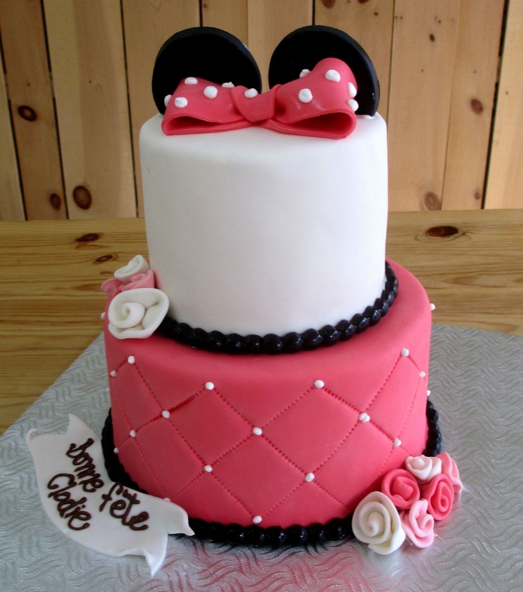 Gâteau d'anniversaire sur mesure de Clodie: gâteau de 2 étages à thématique de Minnie Mouse avec une couverture en fondant rose et blanc, une base rose à effet matelassé (quilting) ornementée de perles blanches et décoré d'oreilles noires et d'une boucle rose à pois blancs.