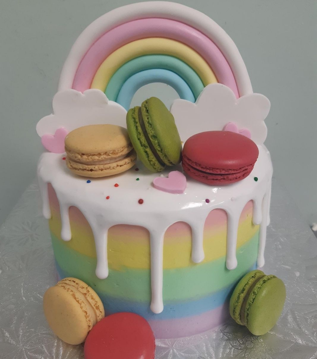 Gâteau d'anniversaire sur mesure: gâteau avec un coulis blanc sur une couverture à la crème au beurre ombrée de couleurs arc-en-ciel et décoré d'un arc-en-ciel en fondant et de macarons.