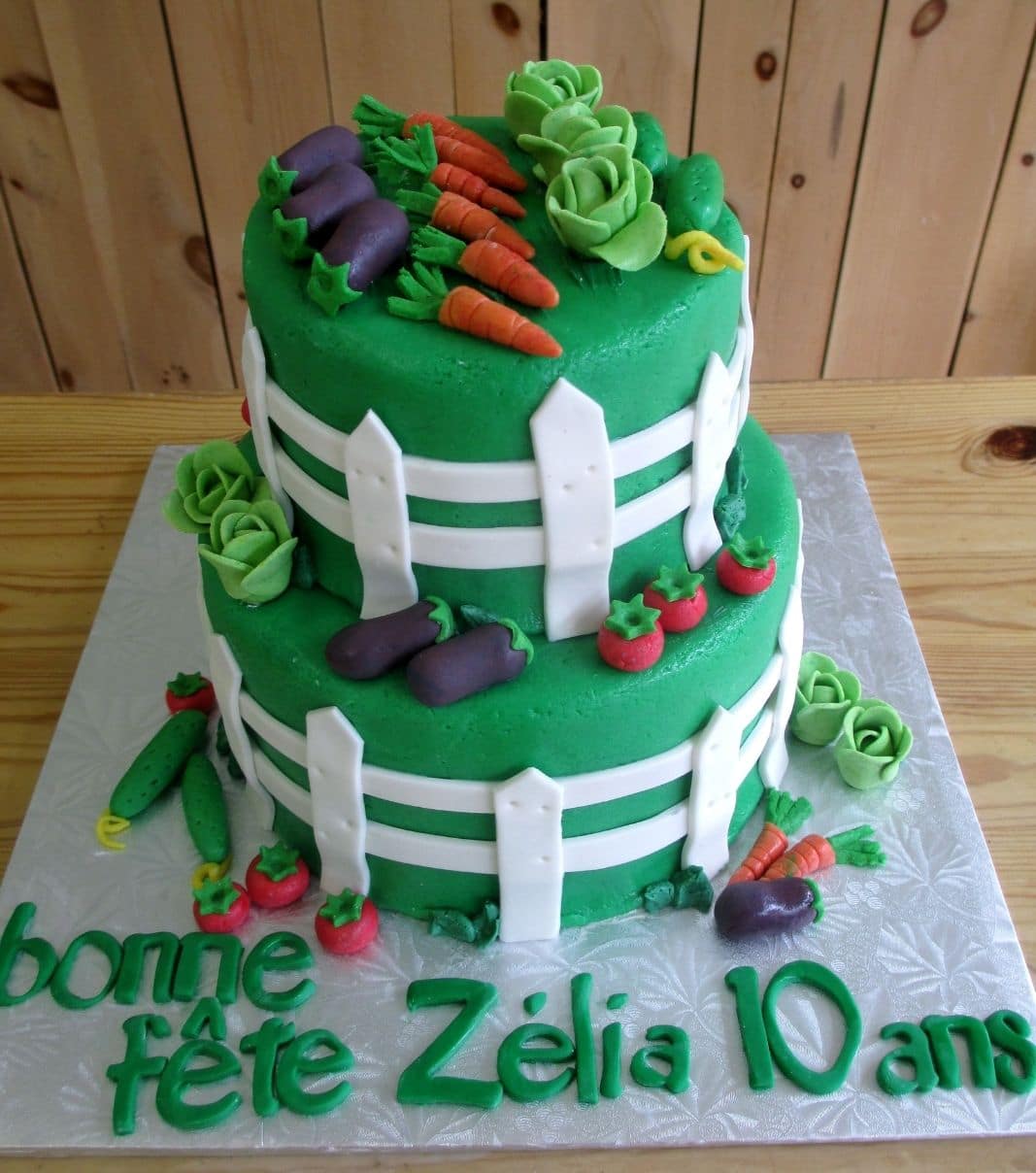 Gâteau d'anniversaire sur mesure de 10 ans de Zélia: gâteau de 2 étages en forme de potager avec une couverture en fondant et décoré d'une clôture et de légumes de jardin (aubergines, carottes, laitues, tomates et concombres) en fondant.