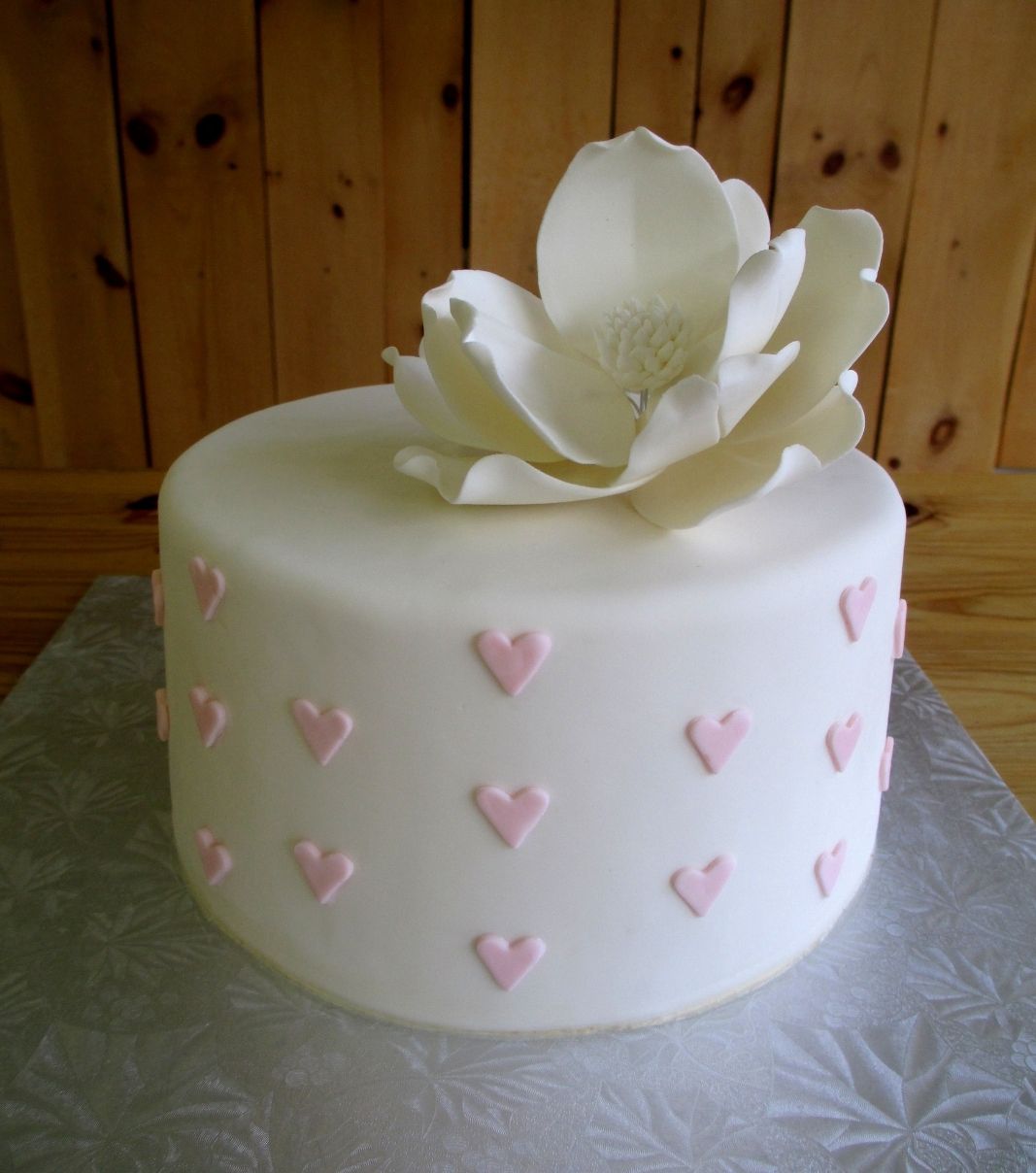 Gâteau d'anniversaire sur mesure: gâteau féminin avec une couverture en fondant blanc ornementé de petits cœurs roses et décoré d'une grosse fleur en sucre.