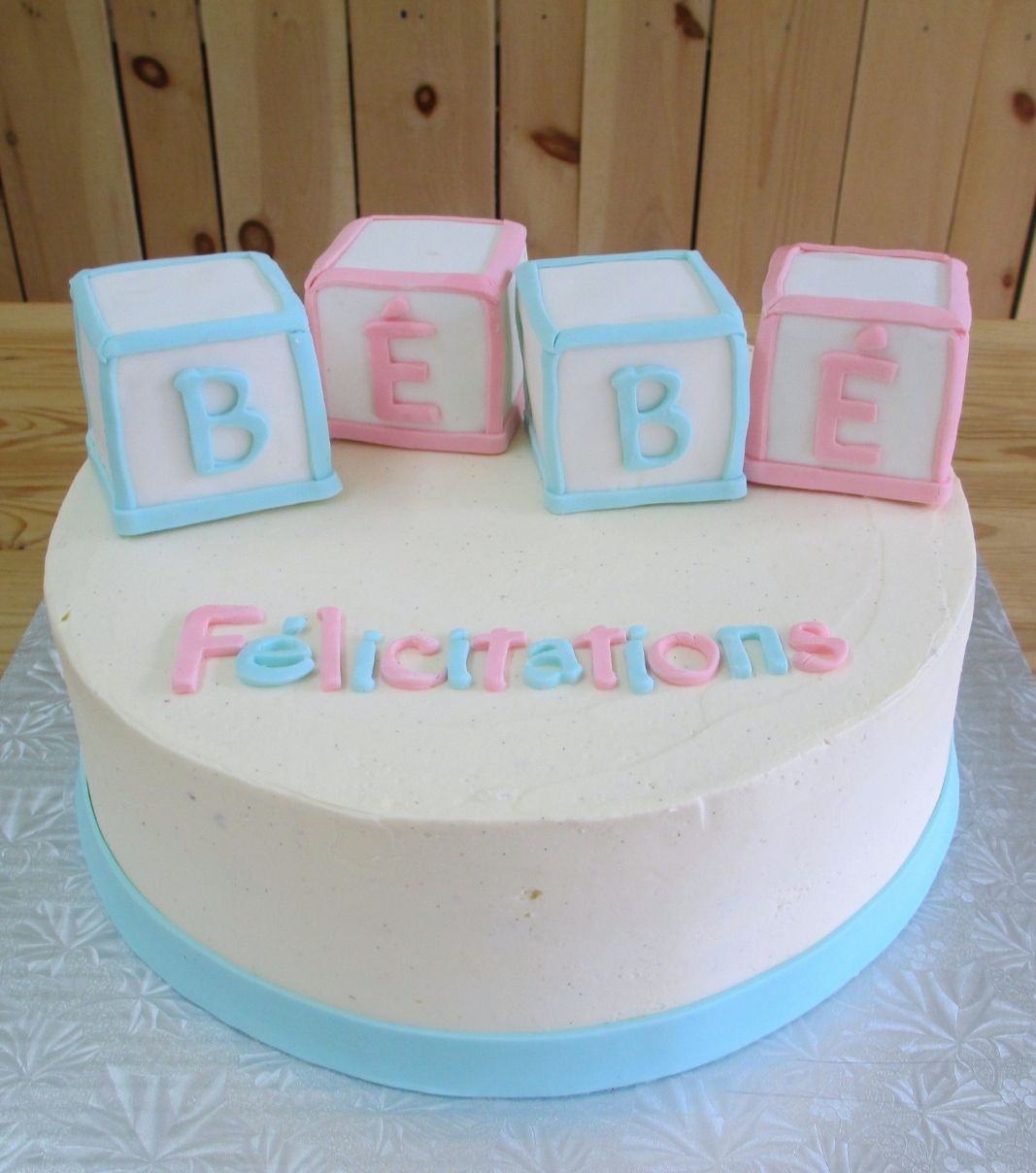 Gâteau shower de bébé: gâteau avec une couverture à la crème au beurre et décoré avec des cubes jouet en fondant avec l'inscription BÉBÉ.