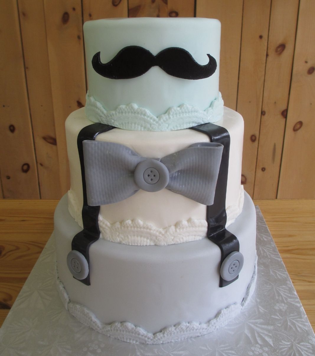 Gâteau shower de bébé garçon: gâteau à thème bleu et gris avec une couverture au fondant et décoré d'une moustache et de bretelles.