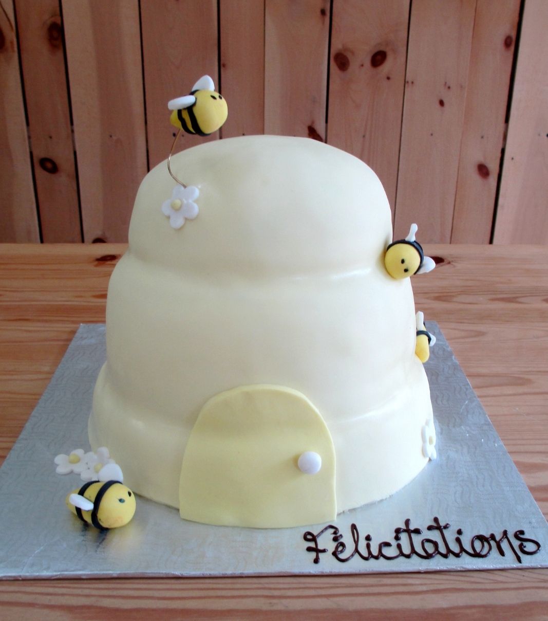 Gâteau shower de bébé: gâteau de 3 étages en forme de ruche 3D avec une couverture en fondant jaune pastel et décoré avec des abeilles sur des fils de fer.