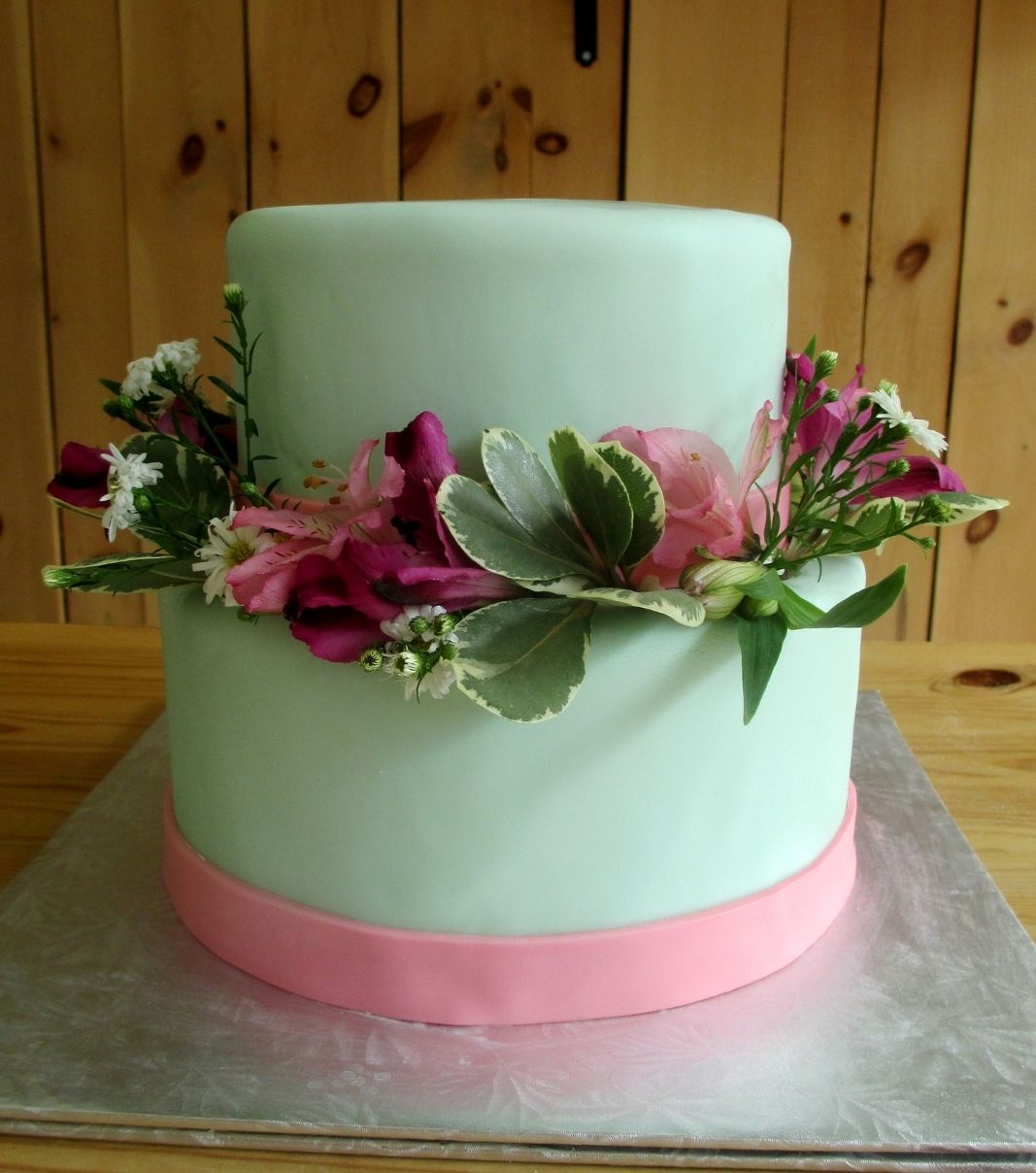 Gâteau d'anniversaire sur mesure: gâteau de 2 étages avec une couverture en fondant vert et rose et décoré de fleurs fraîches.