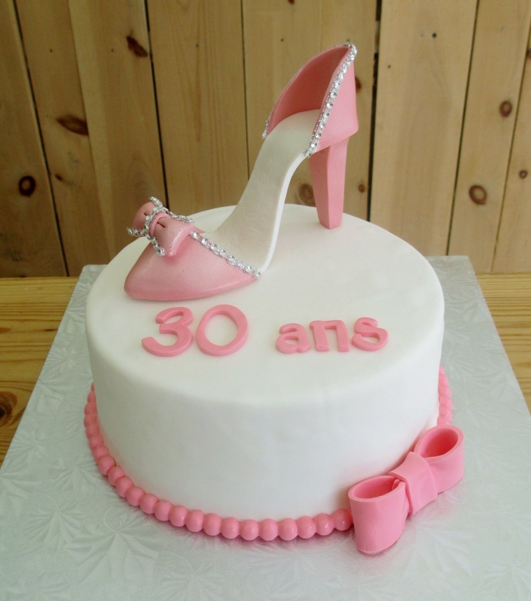 Gâteau d'anniversaire sur mesure de 30 ans: gâteau avec une couverture en fondant et décoré d'un soulier à talon haut rose et d'une boucle rose.