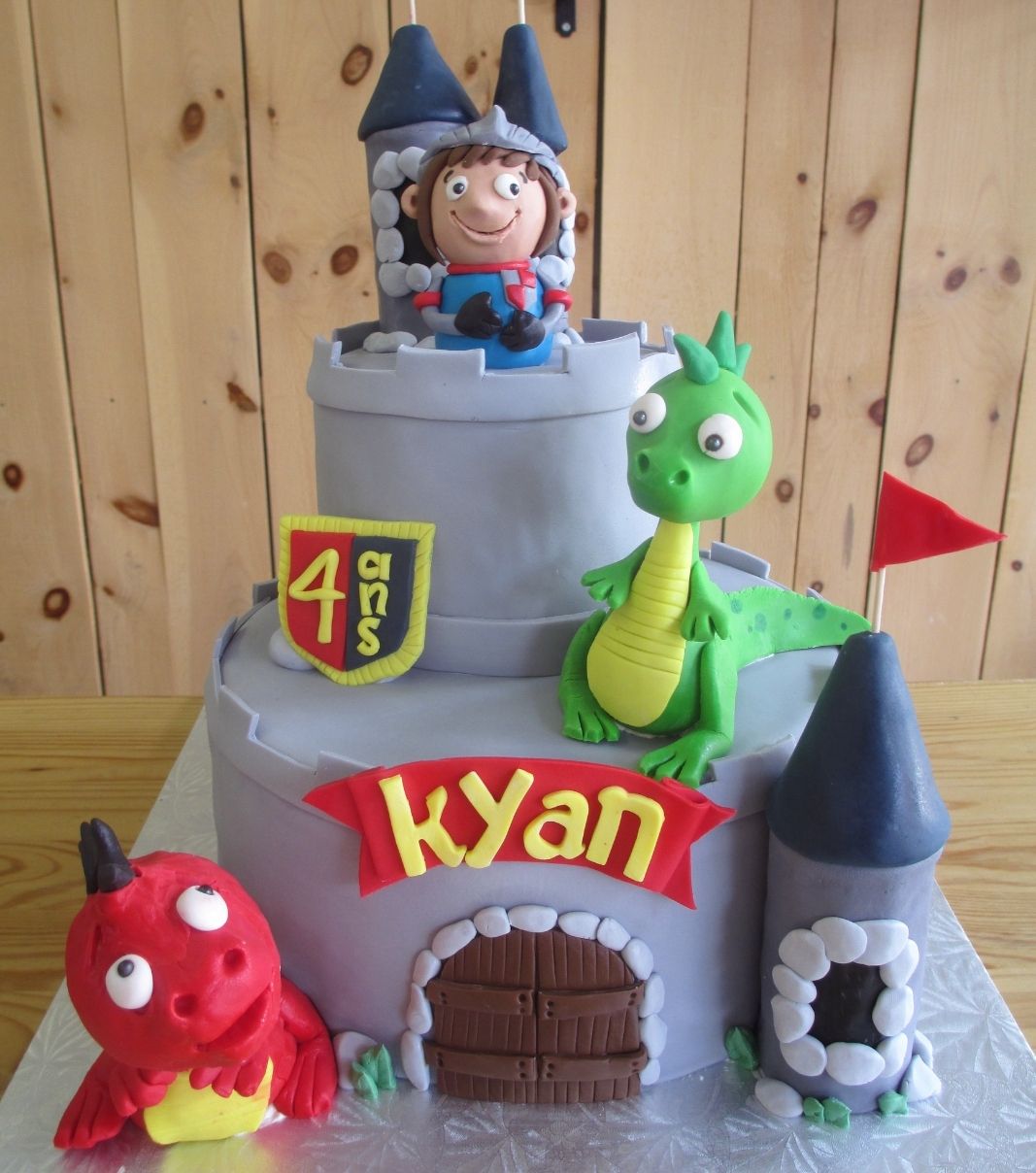 Gâteau d'anniversaire sur mesure des 4 and de Kyan: gâteau de 2 étages à thématique de château avec une couverture en fondant et décoré de figurines 3D de chevalier et de dragons en fondant.