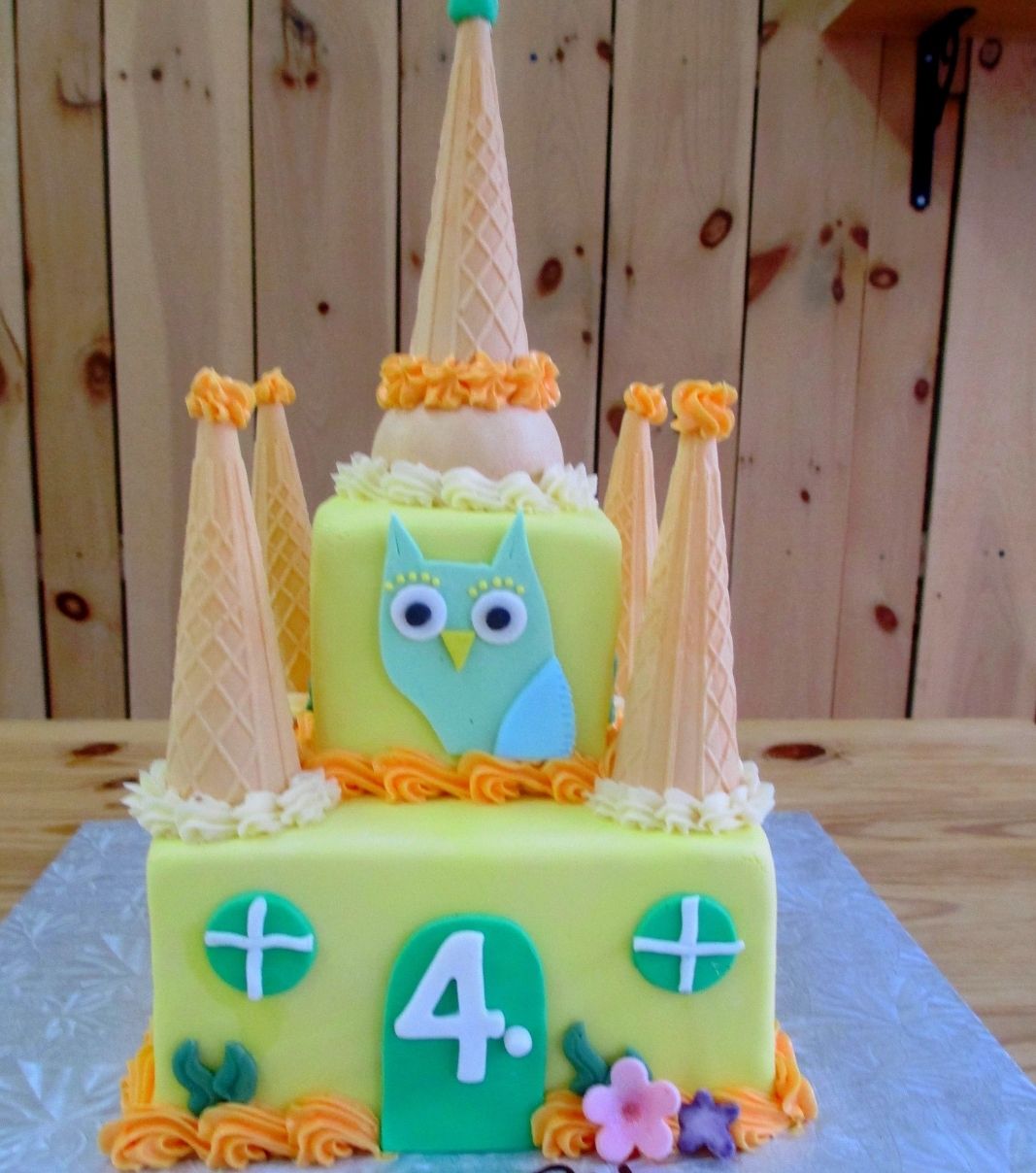 Gâteau d'anniversaire sur mesure des 4 ans d'Éloïse et Antonin: gâteau de 2 étages en forme de château à thématique de hibou avec une couverture en fondant jaune pastel et décoré de cornets de crème glacée.