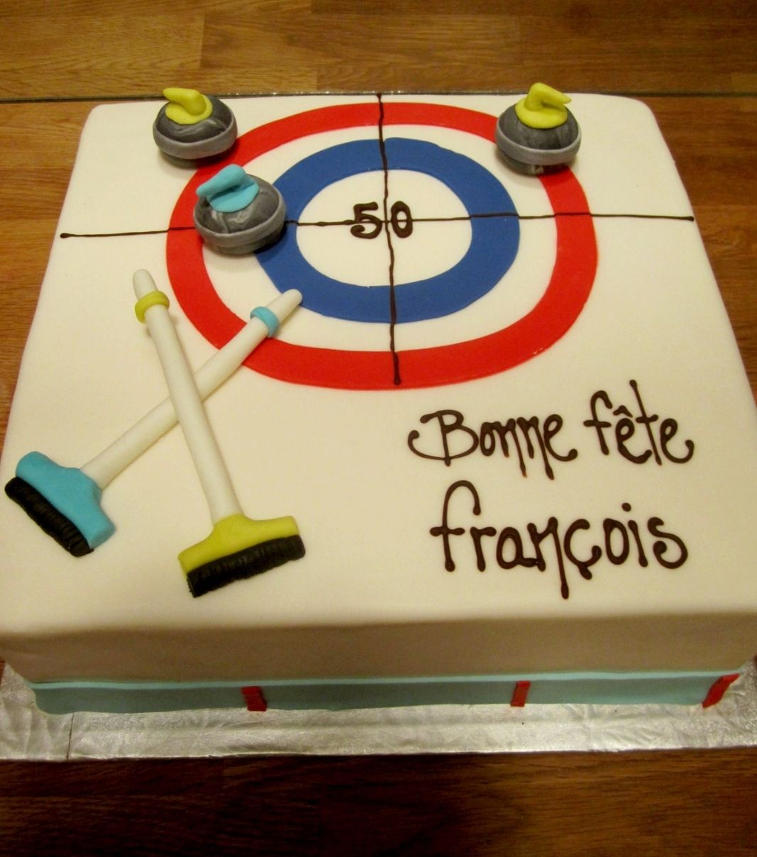 Gâteau d'anniversaire sur mesure des 50 ans de François: gâteau à thématique de curling avec une couverture en fondant et décoré de balais et de pierres de curling en fondant.