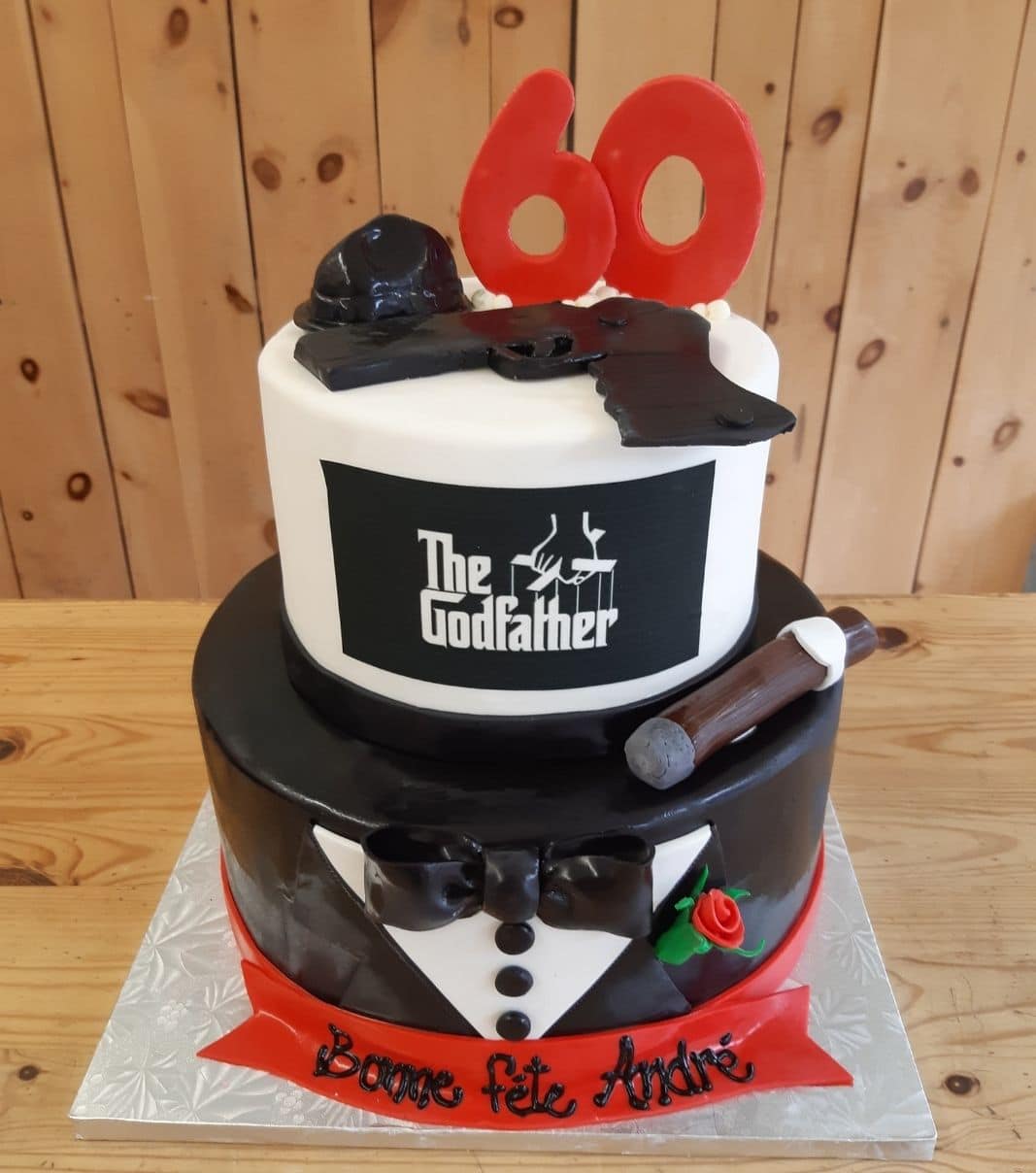 Gâteau d'anniversaire sur mesure de 60 ans d'André: gâteau de 2 étages à thématique Le Parrain avec une couverture en fondant en tuxedo et décoré d'un fusil, d'un cigare et d'un chapeau en fondant.