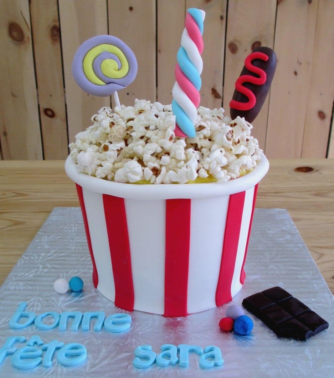 Gâteau d'anniversaire sur mesure de Sara: gâteau en forme de bol de maïs soufflé avec une couverture en fondant et décoré de chocolat, de bonbons et de sucettes en fondant et de popcorn de cinéma.