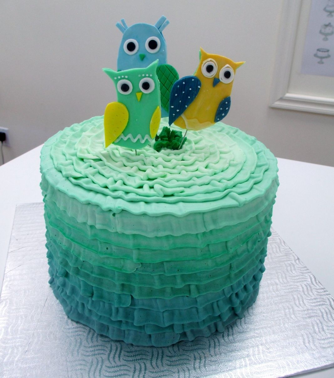 Gâteau d'anniversaire sur mesure: gâteau avec une couverture à la crème au beurre en texture plissée (ruffle) en dégradé turquoise et décoré de hiboux en fondant 2D.