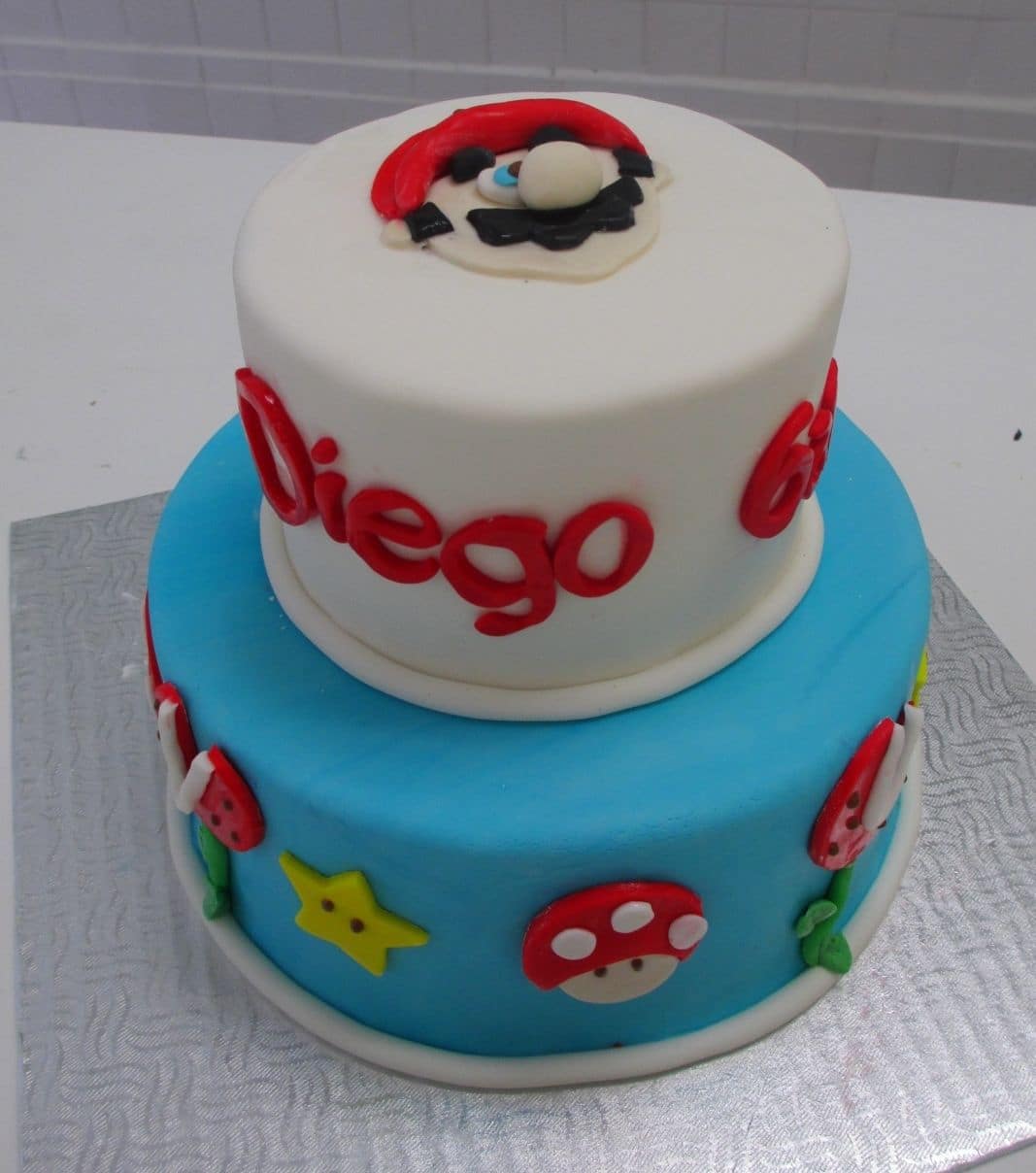 Gâteau d'anniversaire sur mesure de Diego: gâteau de 2 étages à thématique Mario Bros avec une couverture en fondant et décoré de champignons, d'étoiles, de plantes et de Mario en fondant.