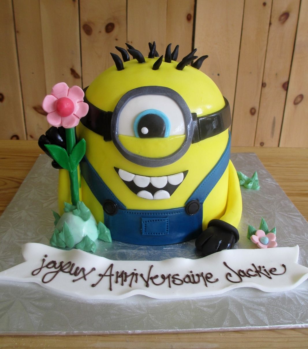 Gâteau d'anniversaire sur mesure de Jackie: gâteau 3D à thématique Minion avec une couverture en fondant et décoré d'une fleur en fondant.