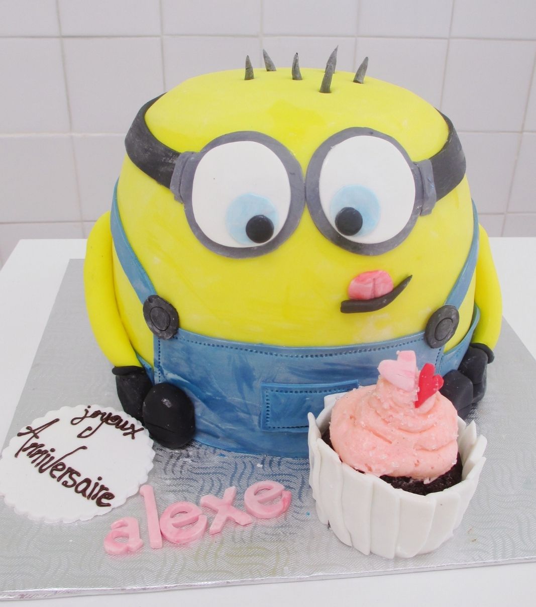 Gâteau d'anniversaire sur mesure de Alexe: gâteau 3D à thématique Minion avec une couverture en fondant et décoré d'un cupcake.