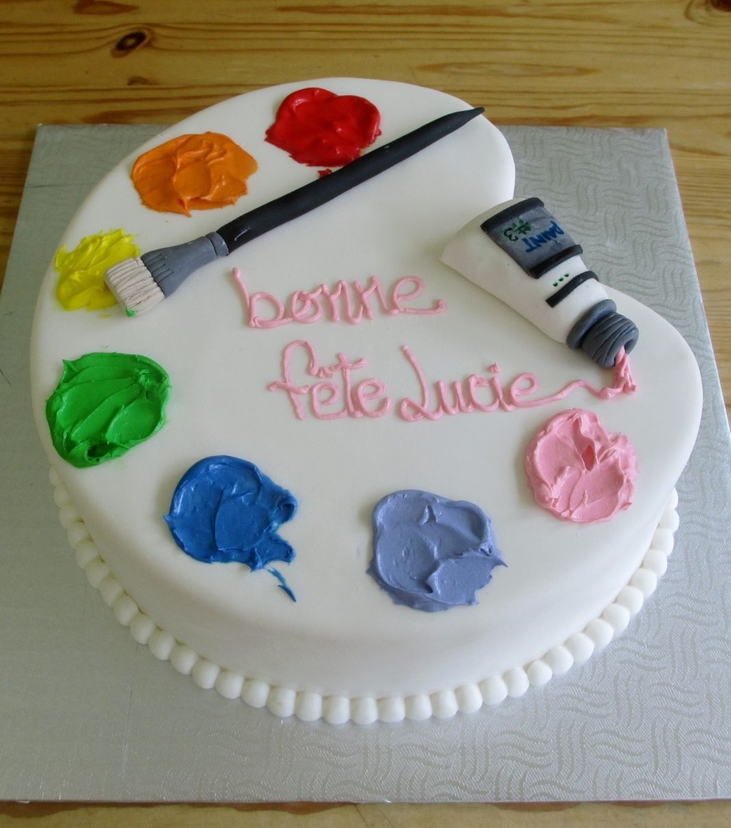 Gâteau d'anniversaire sur mesure de Lucie: gâteau à thématique plateau de peinture avec une couverture en fondant et décoré avec un tube de peinture et un pinceau en fondant et de la peinture en crème au beurre.