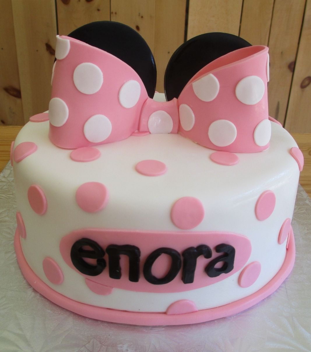 Gâteau d'anniversaire sur mesure d'Enora: gâteau à thématique Minnie Mouse avec une couverture en fondant blanc et rose et décoré d'oreilles noires et d'une boucle rose à pois blancs en fondant.