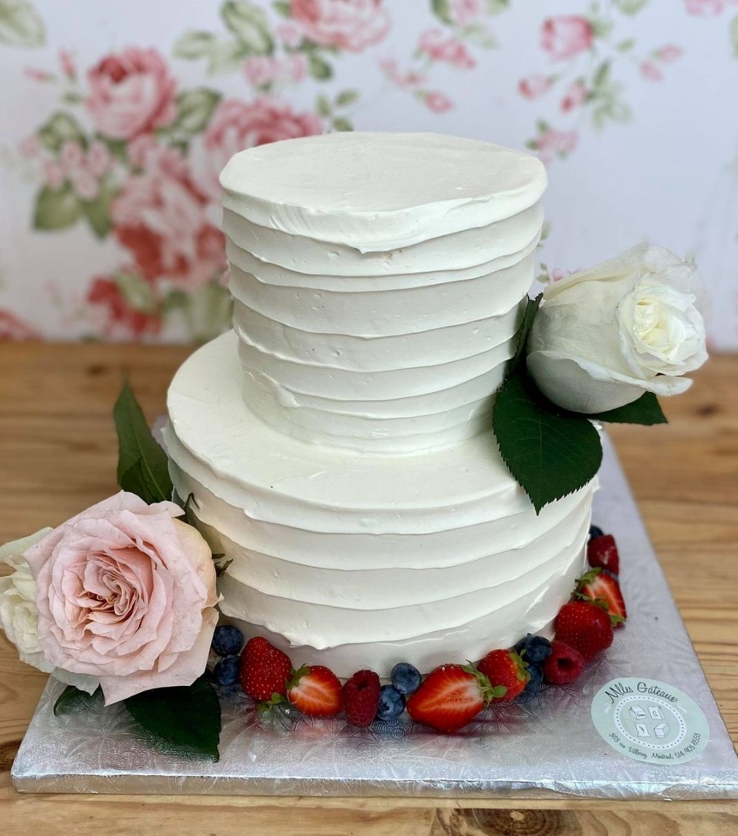 Gâteau de mariage: gâteau de 2 étages avec une couverture effet coup de spatule à la crème au beurre et décoré d'une bordure de fruits frais, de fleurs fraîches et de roses.