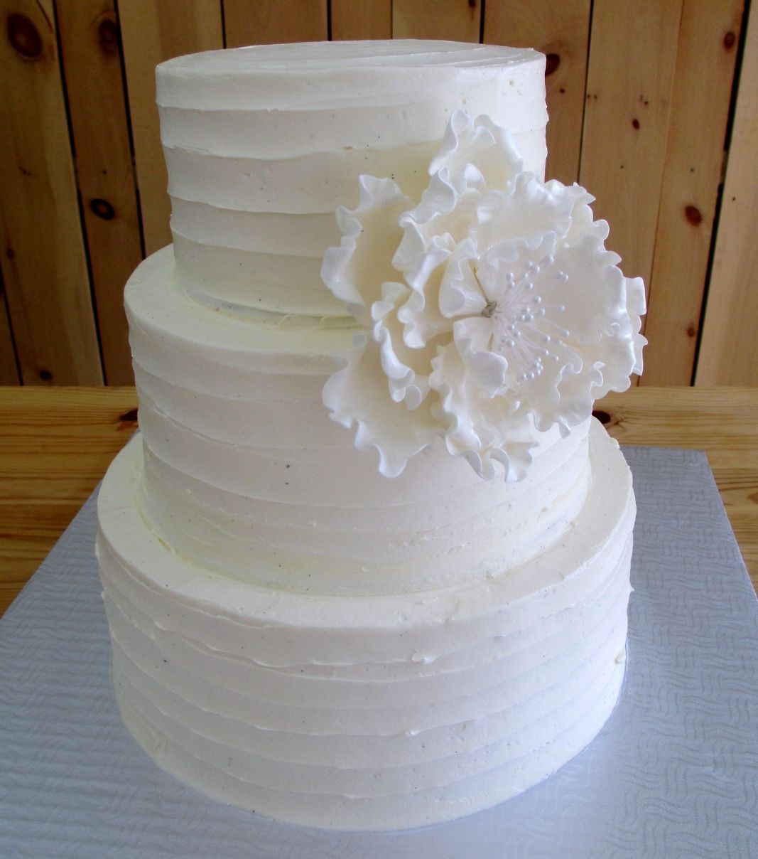Gâteau de mariage: gâteau de 3 étages avec une couverture effet coup de spatule à la crème au beurre et décoré d'une fleur en sucre fondant sculptée à la main.
