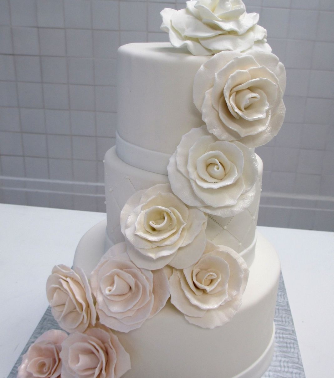 Gâteau de mariage: gâteau de 3 étages avec une couverture au fondant blanc et décoré d'une cascade dégradée de blanc à rose champagne de roses en fondant sculptées à la main.
