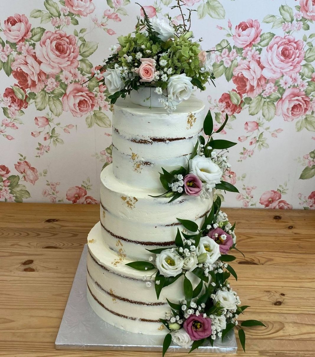 Gâteau de mariage: gâteau de 3 étages de style naked cake, décoré de feuilles d'or et de fleurs fraîches.