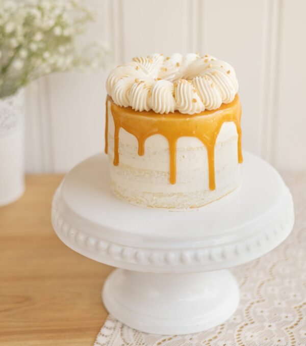 Photo du gâteau d'anniversaire au caramel. Il est masqué finement de crème au beurre. Il y a un coulis caramel sur le dessus ainsi qu'une couronne de crème au beurre.