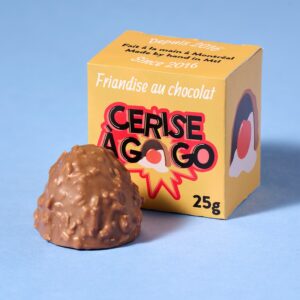Cerise à gogo de la chocolaterie Ernestine. Coque de chocolat au lait à la noix de coco grillée, renfermant une cerise au marasquin plongée dans un fondant crémeux à la vanille. Produit de la sympathique chocolaterie Ernestine à Montréal.